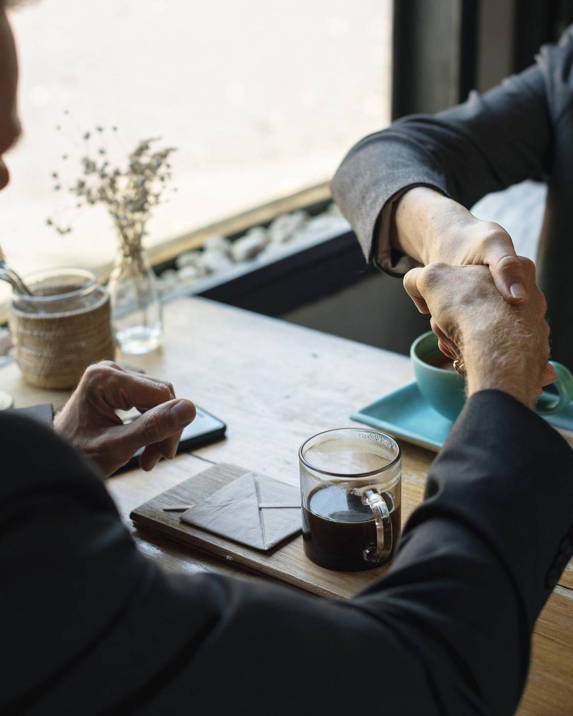 Two people shaking hands over a table in a coffee shop